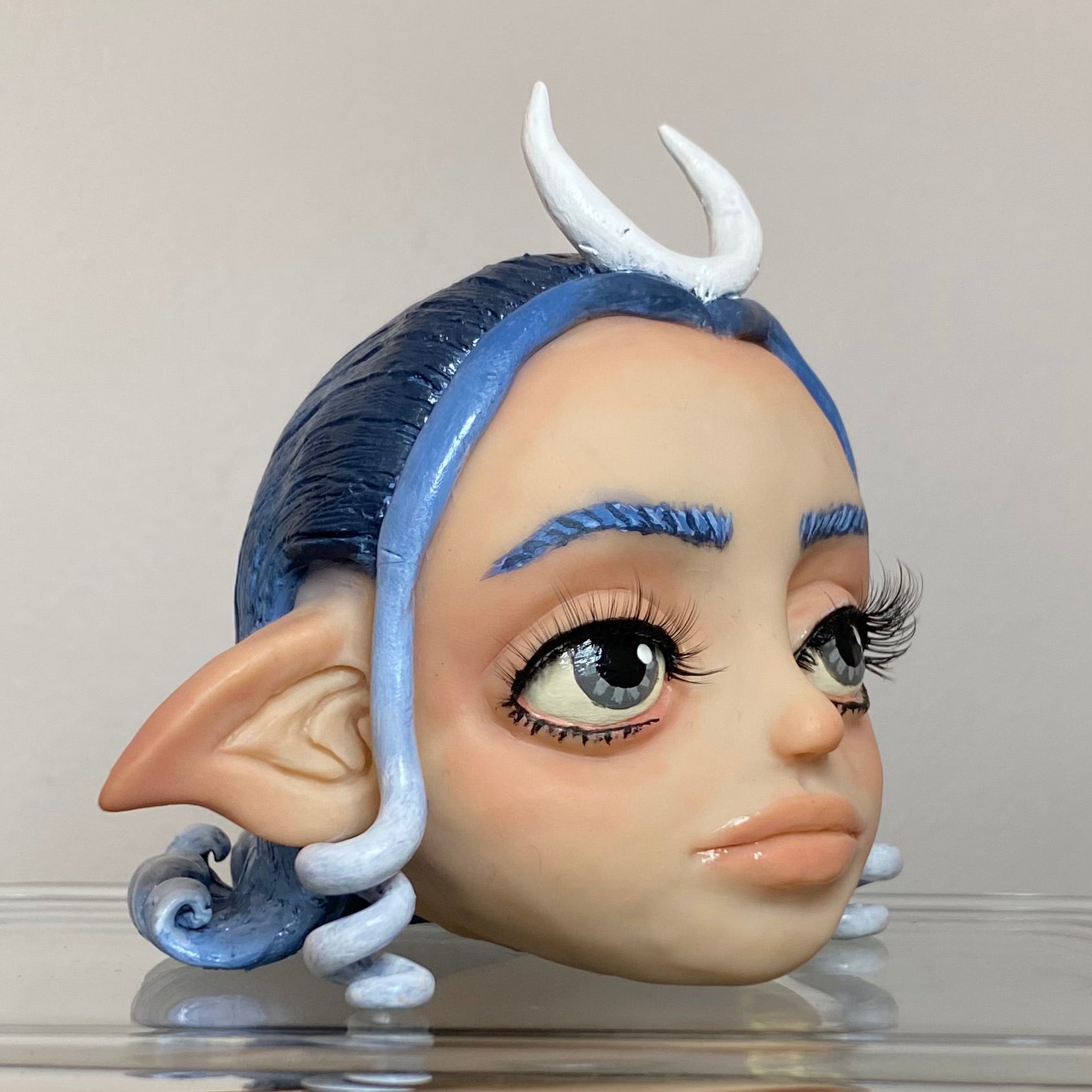 Polymer clay sculpture of a moon elf head, featuring a moon shaped crown, hair in a gradient from dark blue to light blue. 
