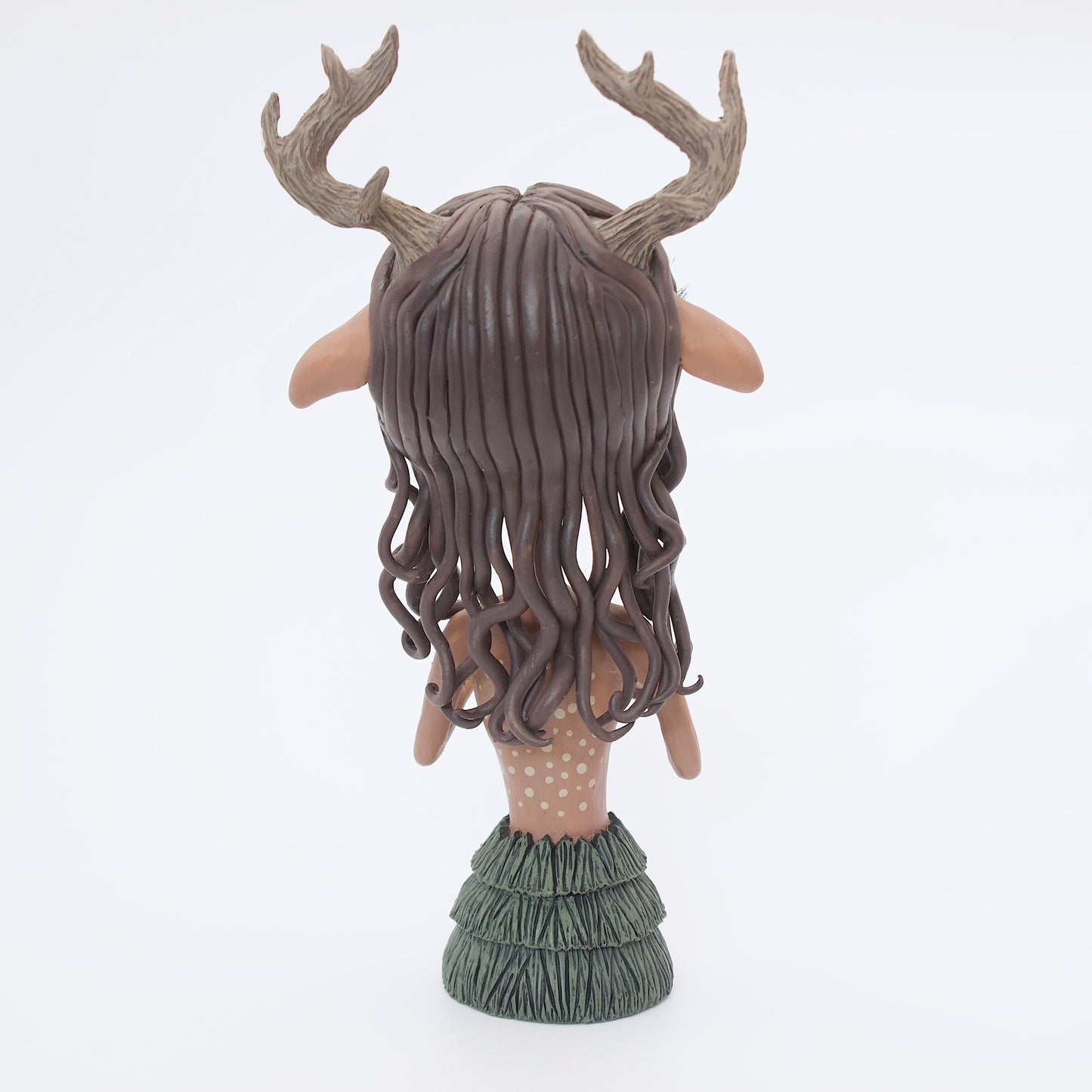 A polymer clay sculpture of a reindeer human hybrid, featuring antlers, a christmas tree skirt, and holly berries and leaves for the top. Also with the iconic Rudolph red nose and deer like ears and hooves.