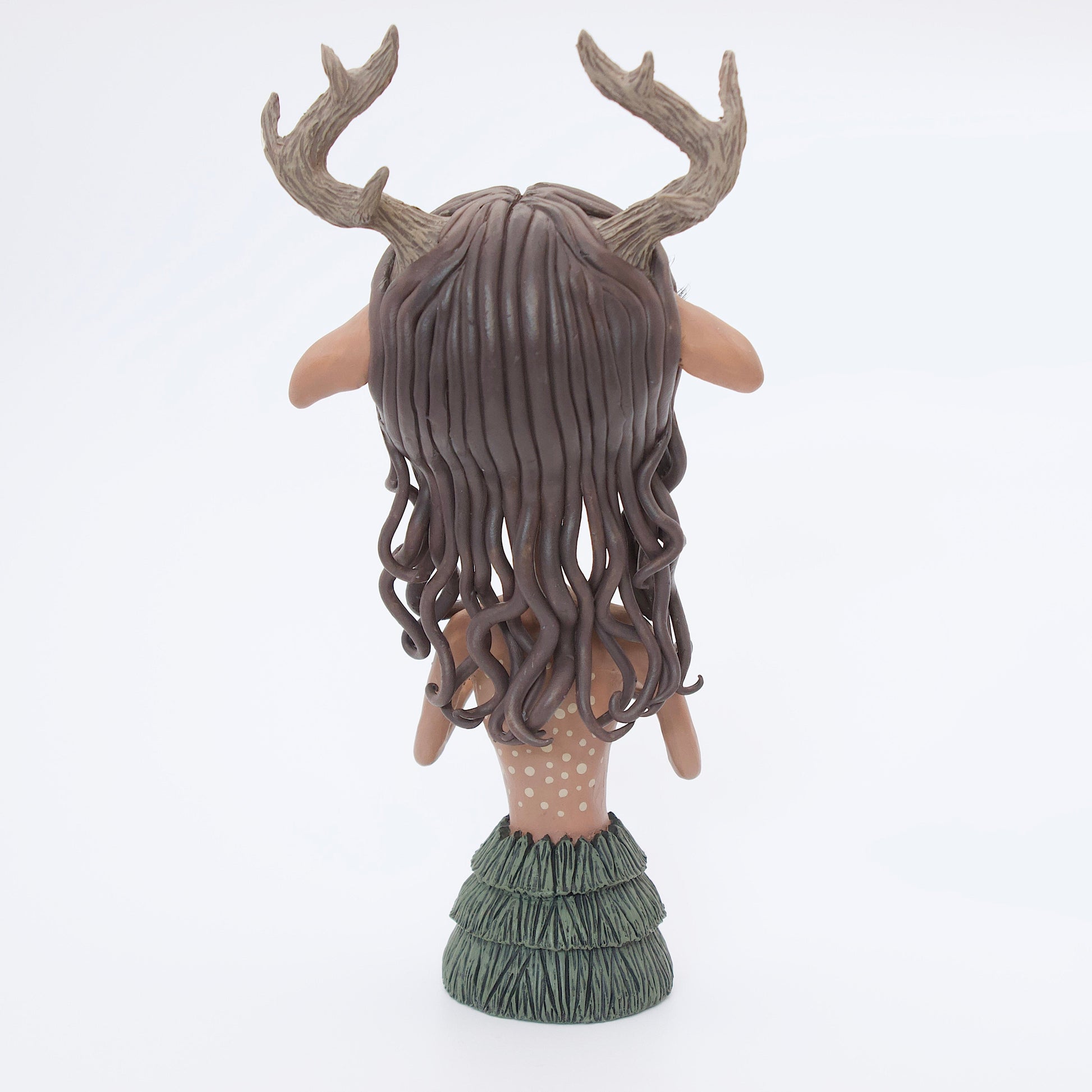 A polymer clay sculpture of a reindeer human hybrid, featuring antlers, a christmas tree skirt, and holly berries and leaves for the top. Also with the iconic Rudolph red nose and deer like ears and hooves.