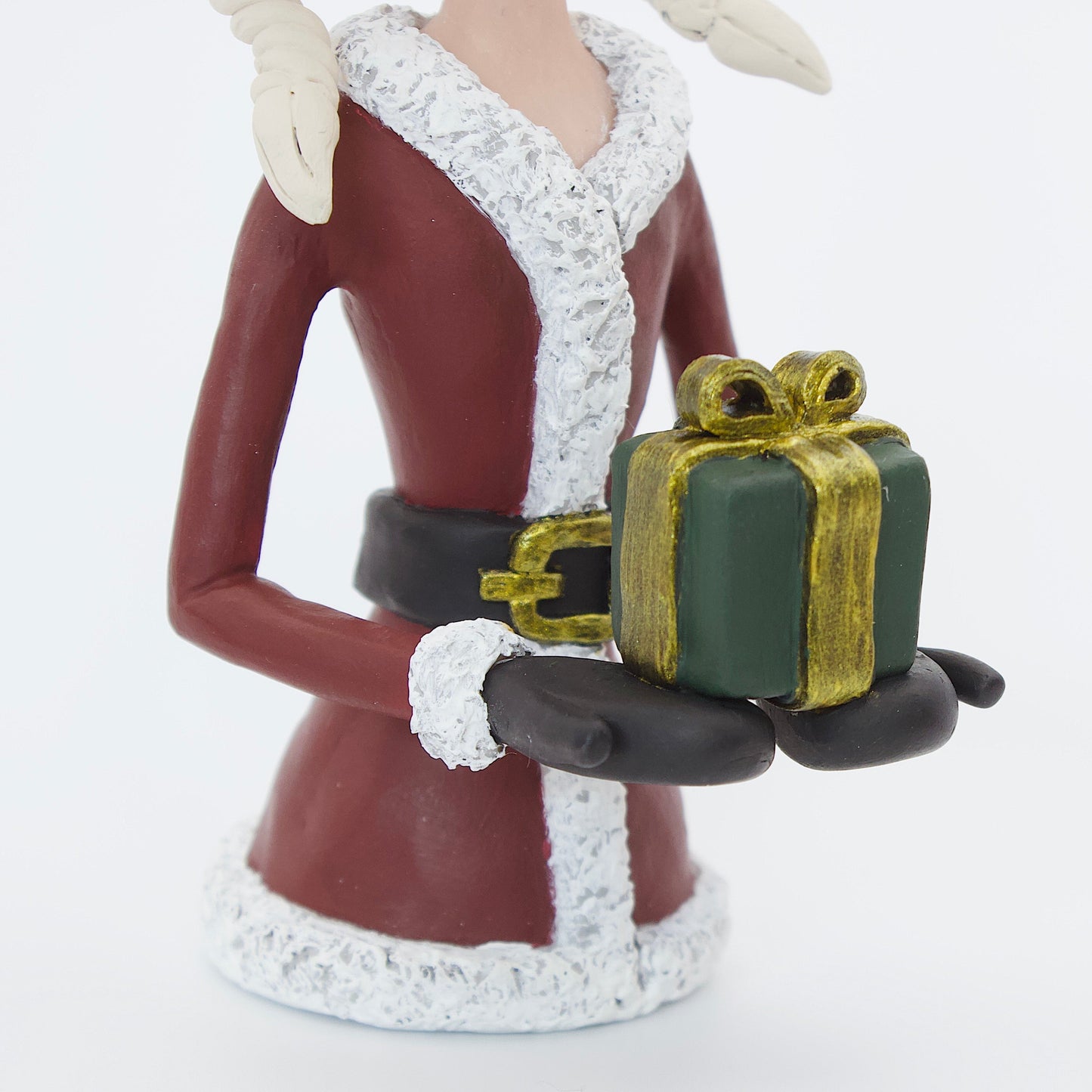 A polymer clay sculpture featuring a young mrs claus with blond hair holding a Christmas present gift box, wearing a Santa hat and suit. 