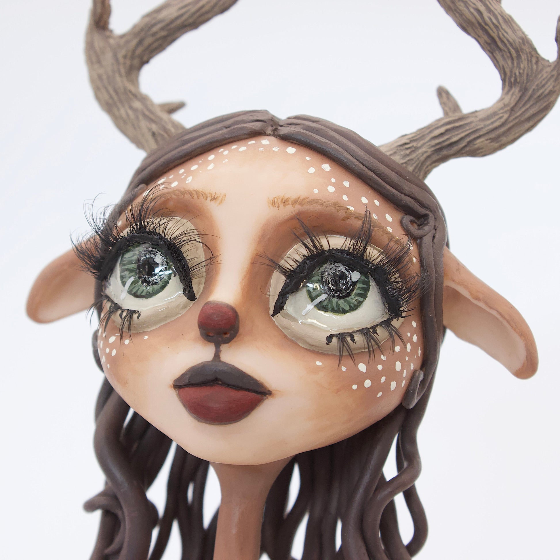 A polymer clay sculpture of a reindeer human hybrid, featuring antlers, a christmas tree skirt, and holly berries and leaves for the top. Also with the iconic Rudolph red nose and deer like ears and hooves.