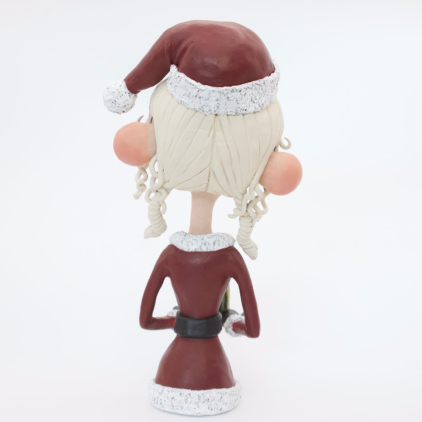 A polymer clay sculpture featuring a young mrs claus with blond hair holding a Christmas present gift box, wearing a Santa hat and suit. 