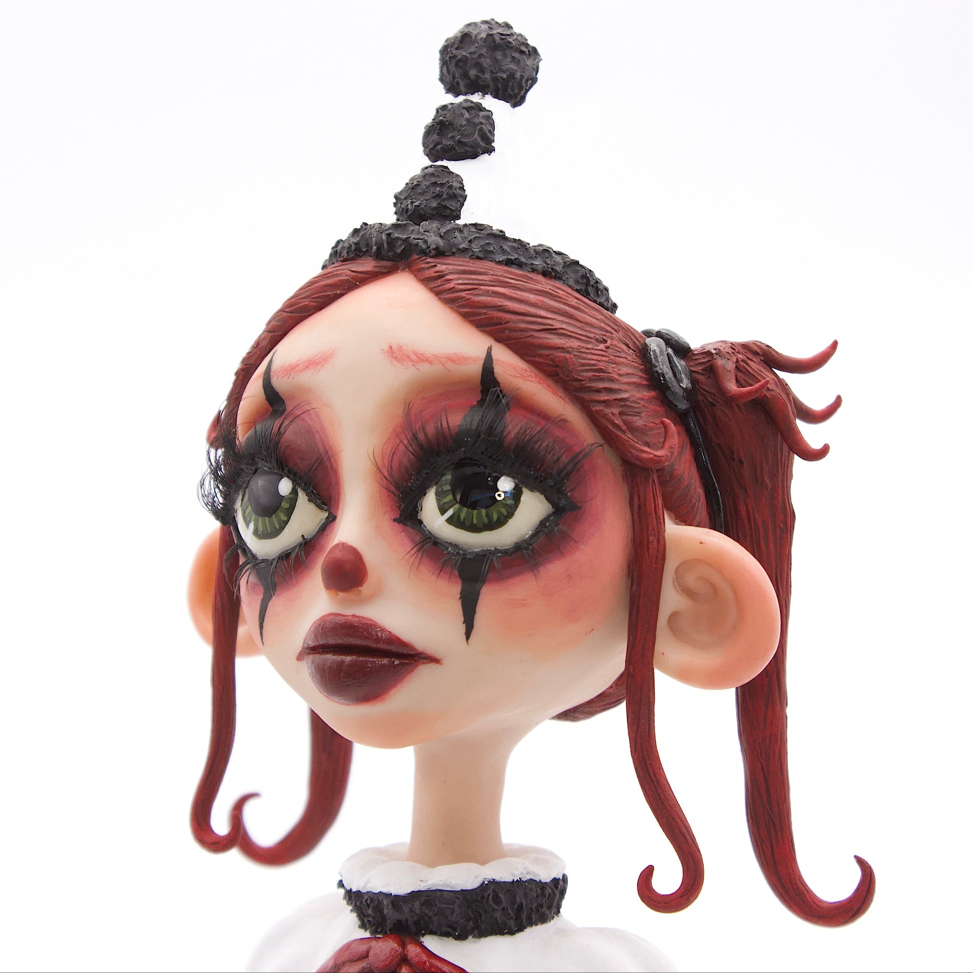 A polymer clay sculpture of a sad pierrot girl clown, holding a drooping rose, wearing the iconic pierrot clown garb in black white and red.