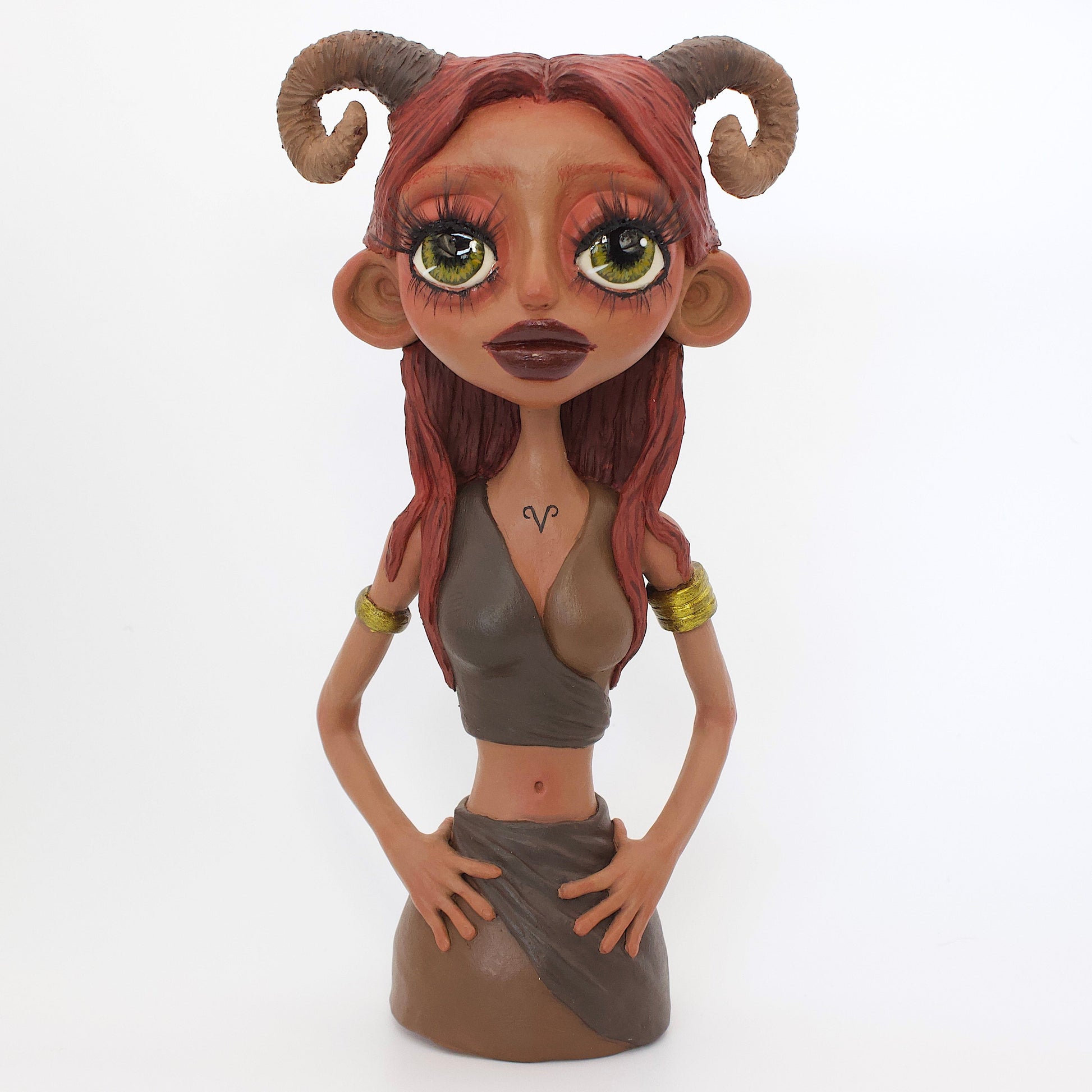 A polymer clay sculpture of the Aries zodiac personified as a woman, featuring red toned browns, long red brown hair and the iconic ram horns.