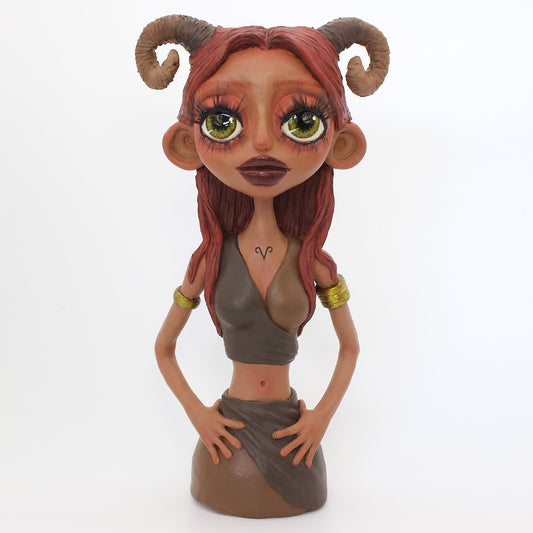 A polymer clay sculpture of the Aries zodiac personified as a woman, featuring red toned browns, long red brown hair and the iconic ram horns.