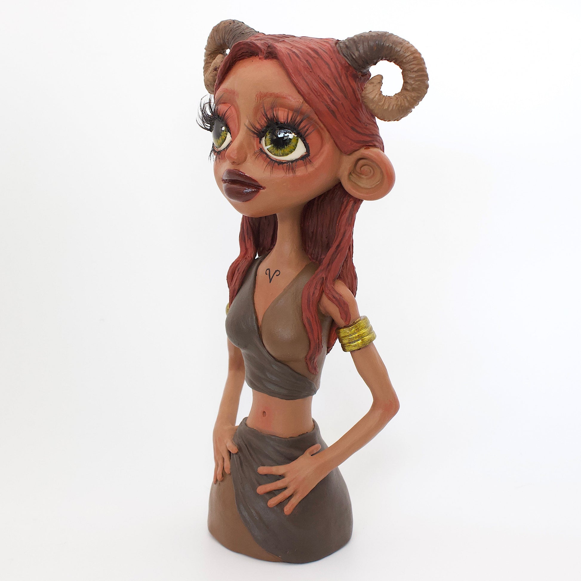 A polymer clay sculpture of the Aries zodiac personified as a woman, featuring red toned browns, long red brown hair and the iconic ram horns.