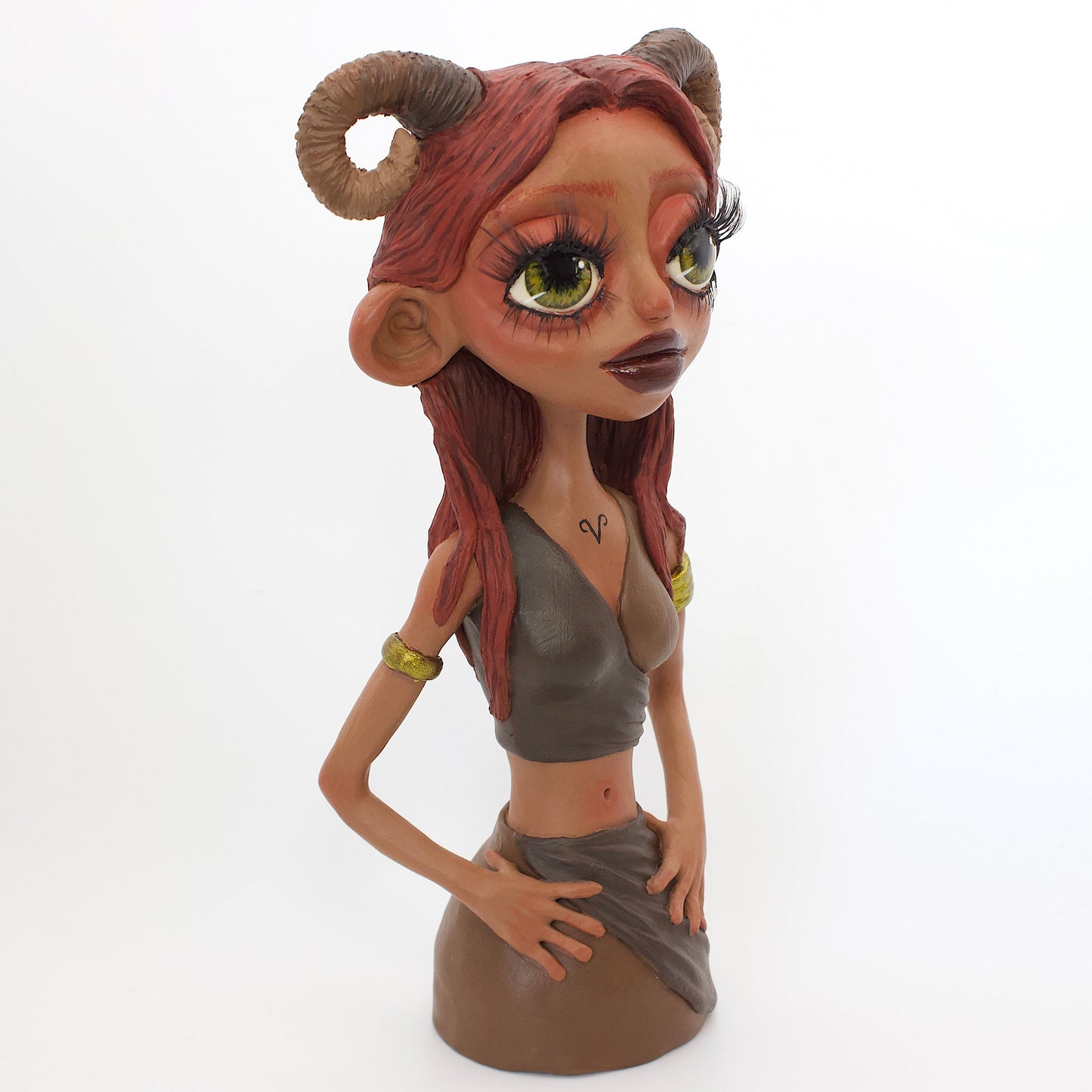 A polymer clay sculpture of the Aries zodiac personified as a woman, featuring red toned browns, long red brown hair and the iconic ram horns.