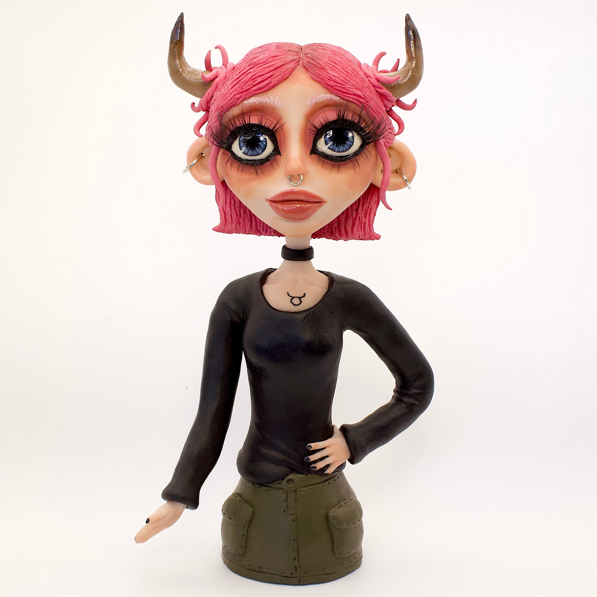 A polymer clay sculpture of the Taurus zodiac personified as a woman, featuring the iconic bull horns, pink hair and grunge/goth piercings, makeup and outfit.