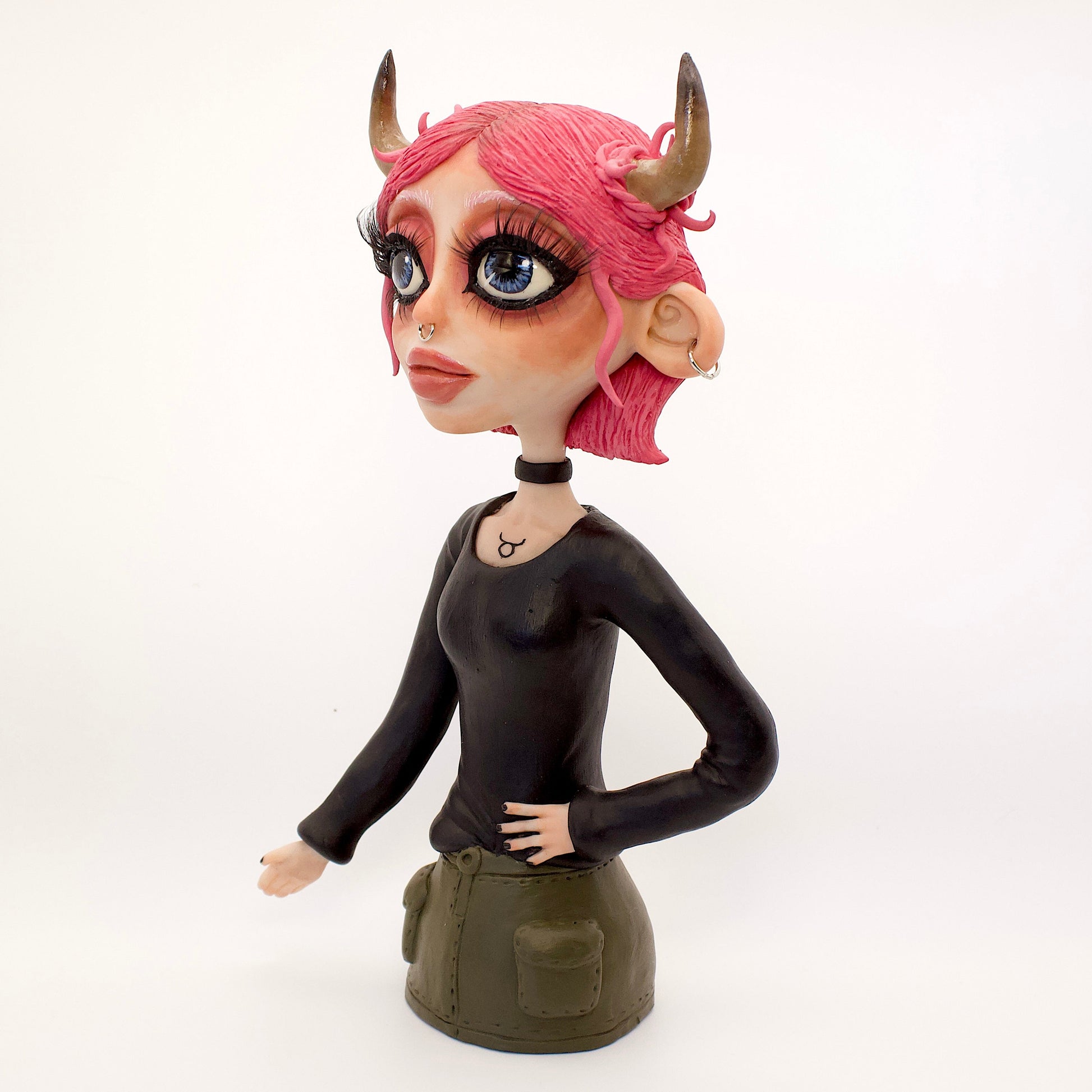 A polymer clay sculpture of the Taurus zodiac personified as a woman, featuring the iconic bull horns, pink hair and grunge/goth piercings, makeup and outfit.