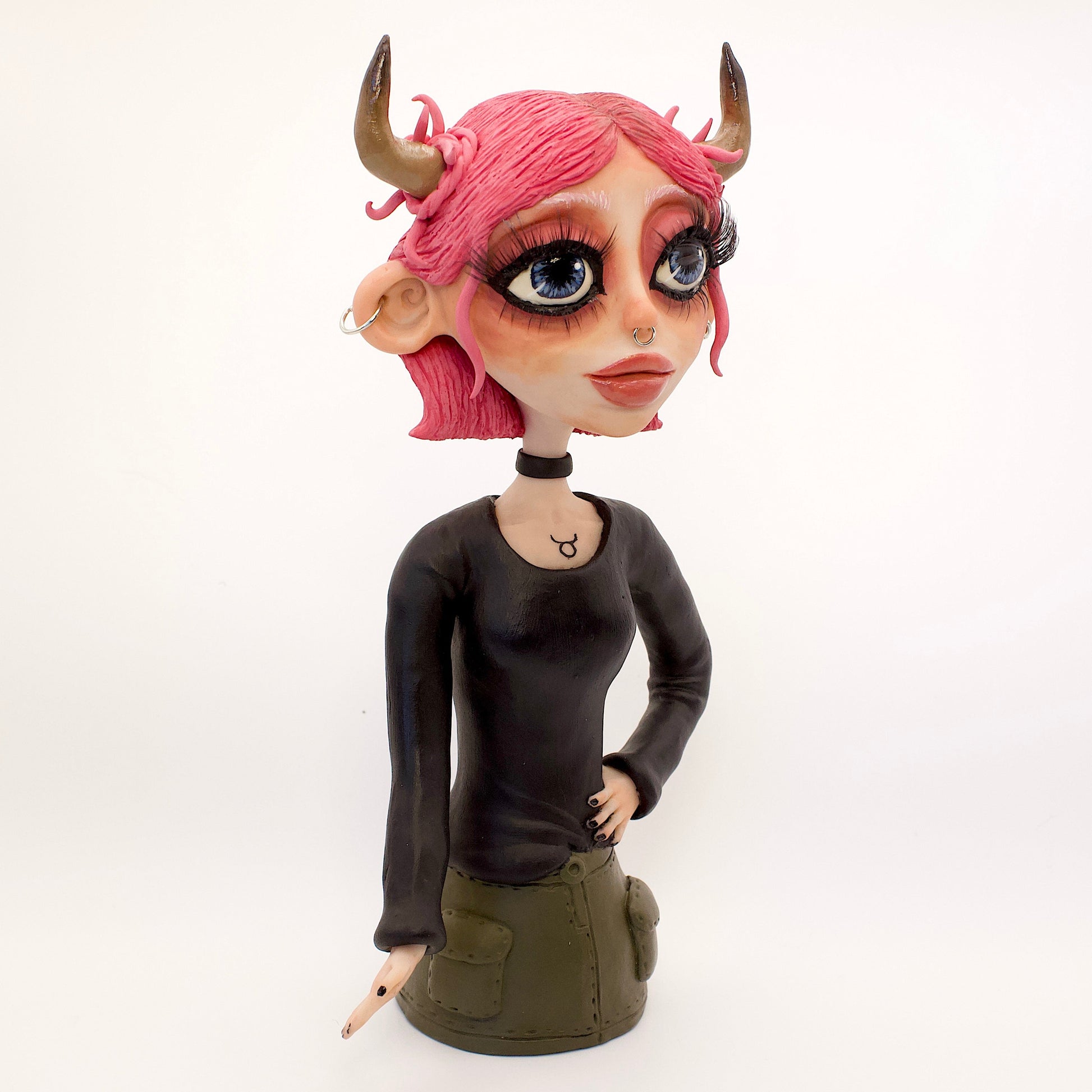 A polymer clay sculpture of the Taurus zodiac personified as a woman, featuring the iconic bull horns, pink hair and grunge/goth piercings, makeup and outfit.