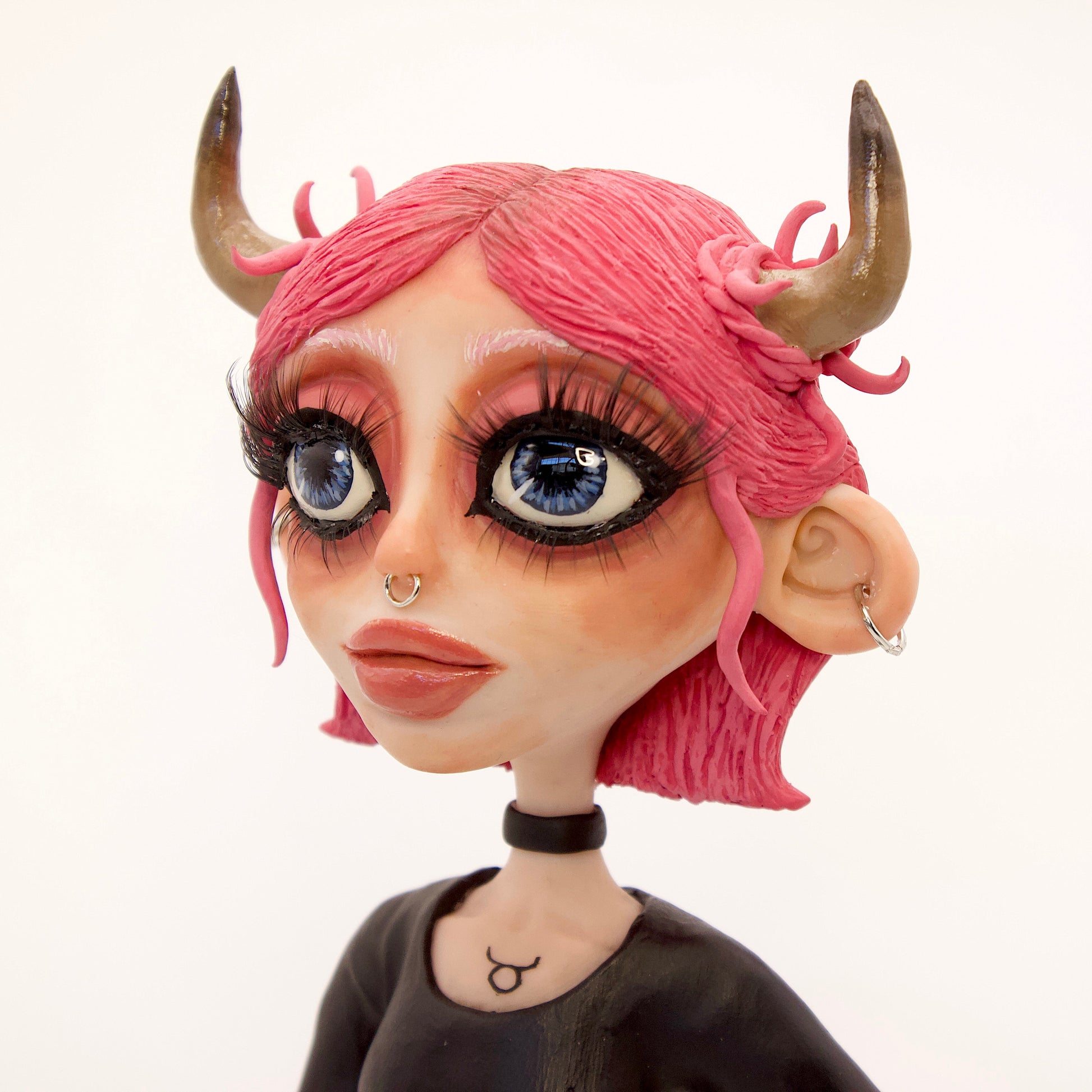 A polymer clay sculpture of the Taurus zodiac personified as a woman, featuring the iconic bull horns, pink hair and grunge/goth piercings, makeup and outfit.