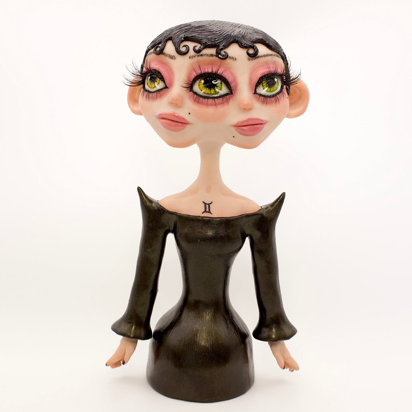 A polymer clay sculpture of the Gemini zodiac personified as a woman, featuring a sleek black dress and two heads fused together, sharing an eye.