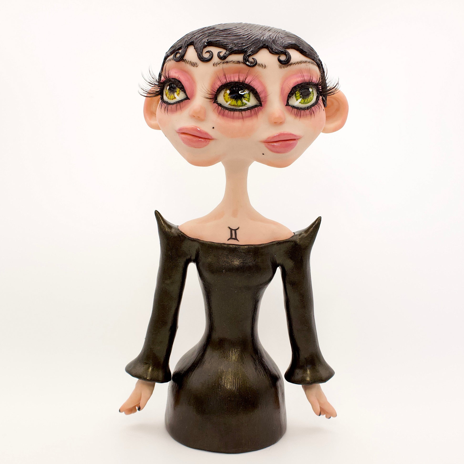 A polymer clay sculpture of the Gemini zodiac personified as a woman, featuring a sleek black dress and two heads fused together, sharing an eye.