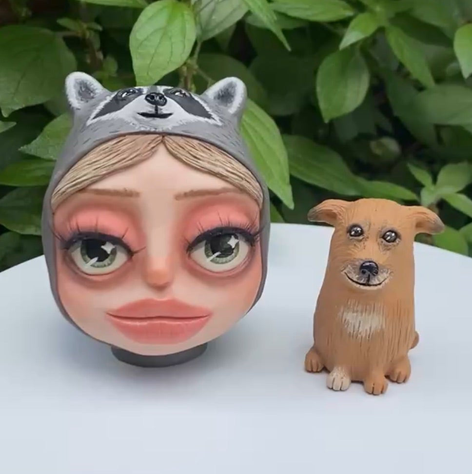 A commissioned polymer clay sculpture of a girl wearing a raccoon beanie and her dog.