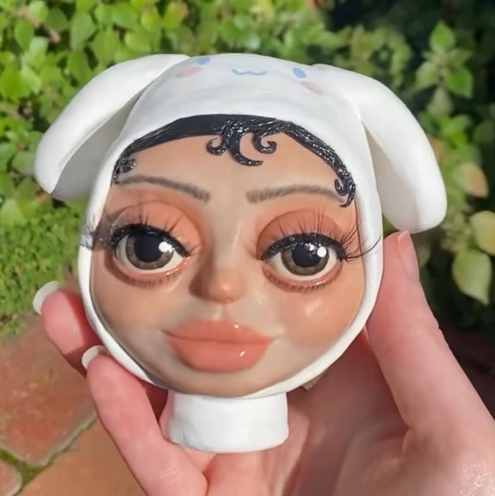 A polymer clay art sculpture of Vanilla Mace's head in a cinamoroll beanie and her two cats, Miso and Chai.