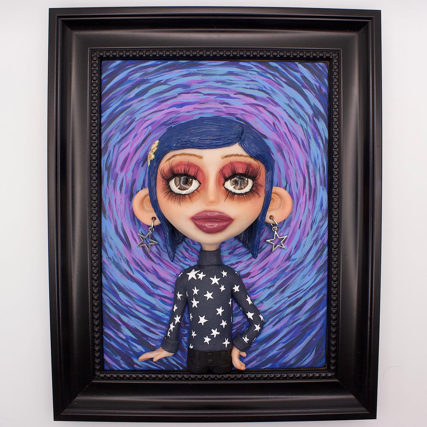 A polymer clay sculpture positioned in a black wood photo frame. Featuring Coraline in her iconic blue star sweater, set against an impressionistic view of the tunnel to the other world. 