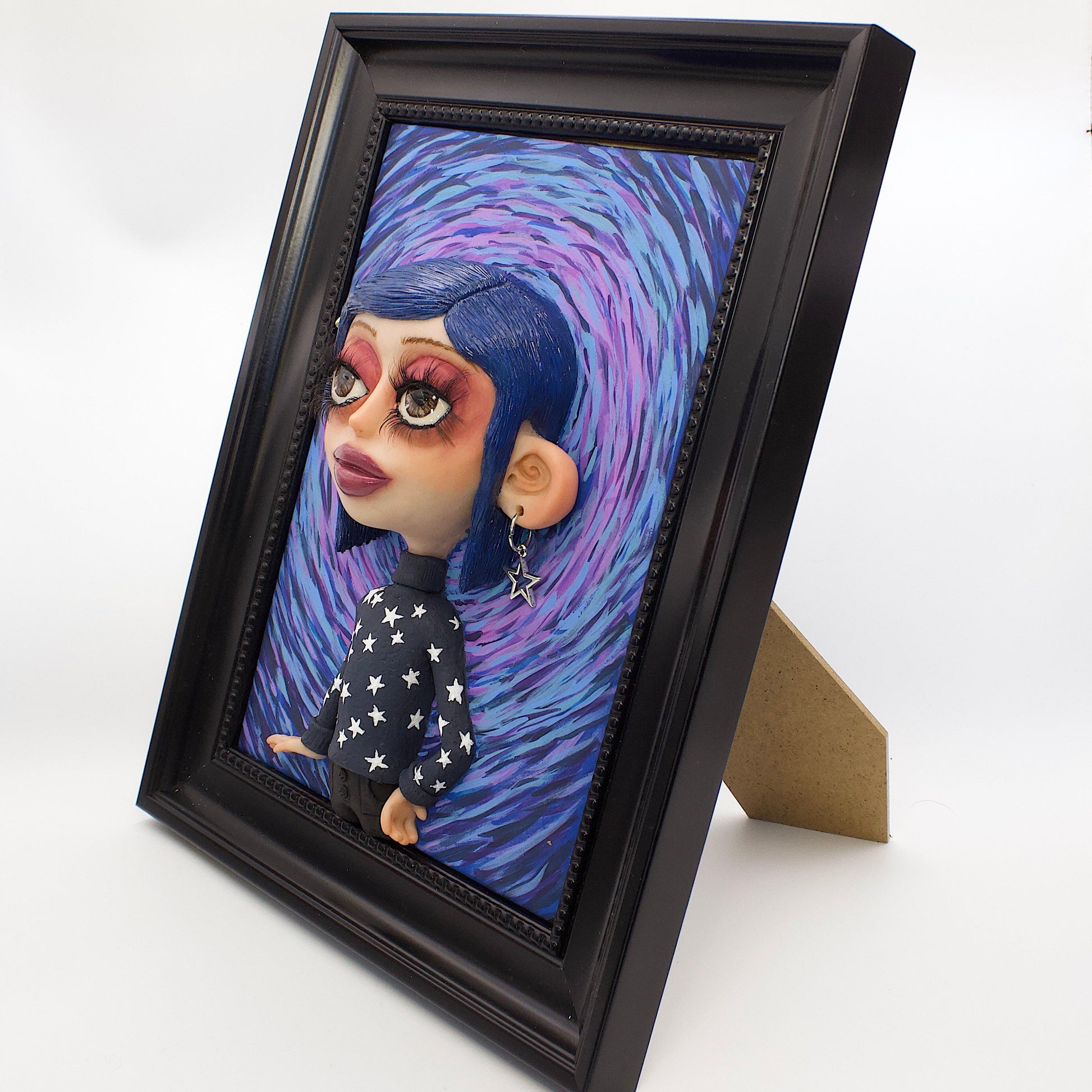A polymer clay sculpture positioned in a black wood photo frame. Featuring Coraline in her iconic blue star sweater, set against an impressionistic view of the tunnel to the other world. 