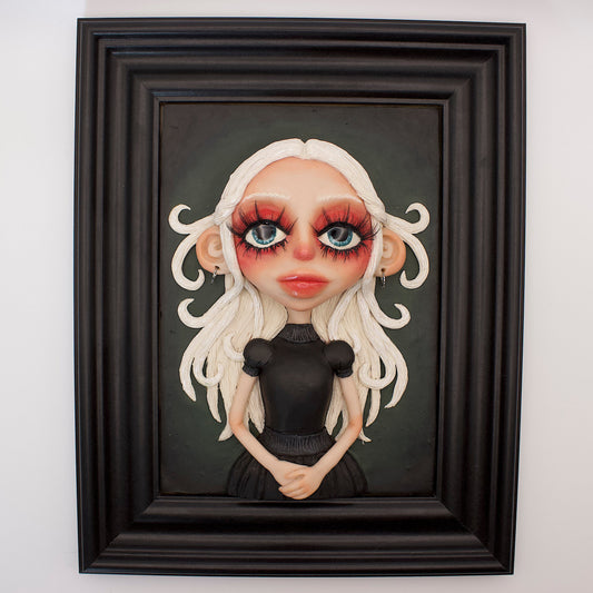 A polymer clay sculpture positioned in a black wood photo frame. Featuring a haunting girl with blond hair and a black Victorian style gothic dress, set against a green black gradient background. 